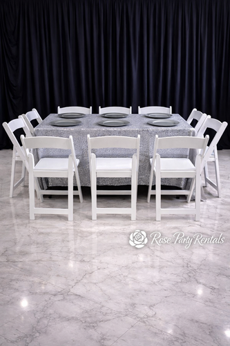 White folding chairs around rectangular table with silver linen and chargers